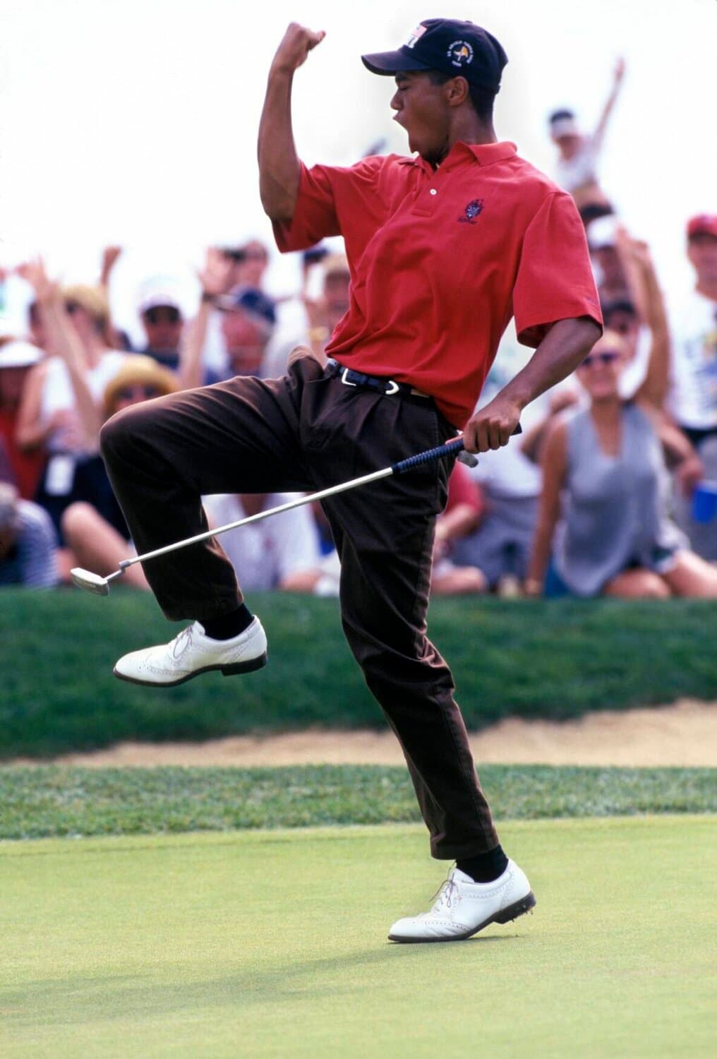 Tiger Woods celebrates a putt at the 1996 US Amateur, one knee raised, wearing white wingtip golf shoes